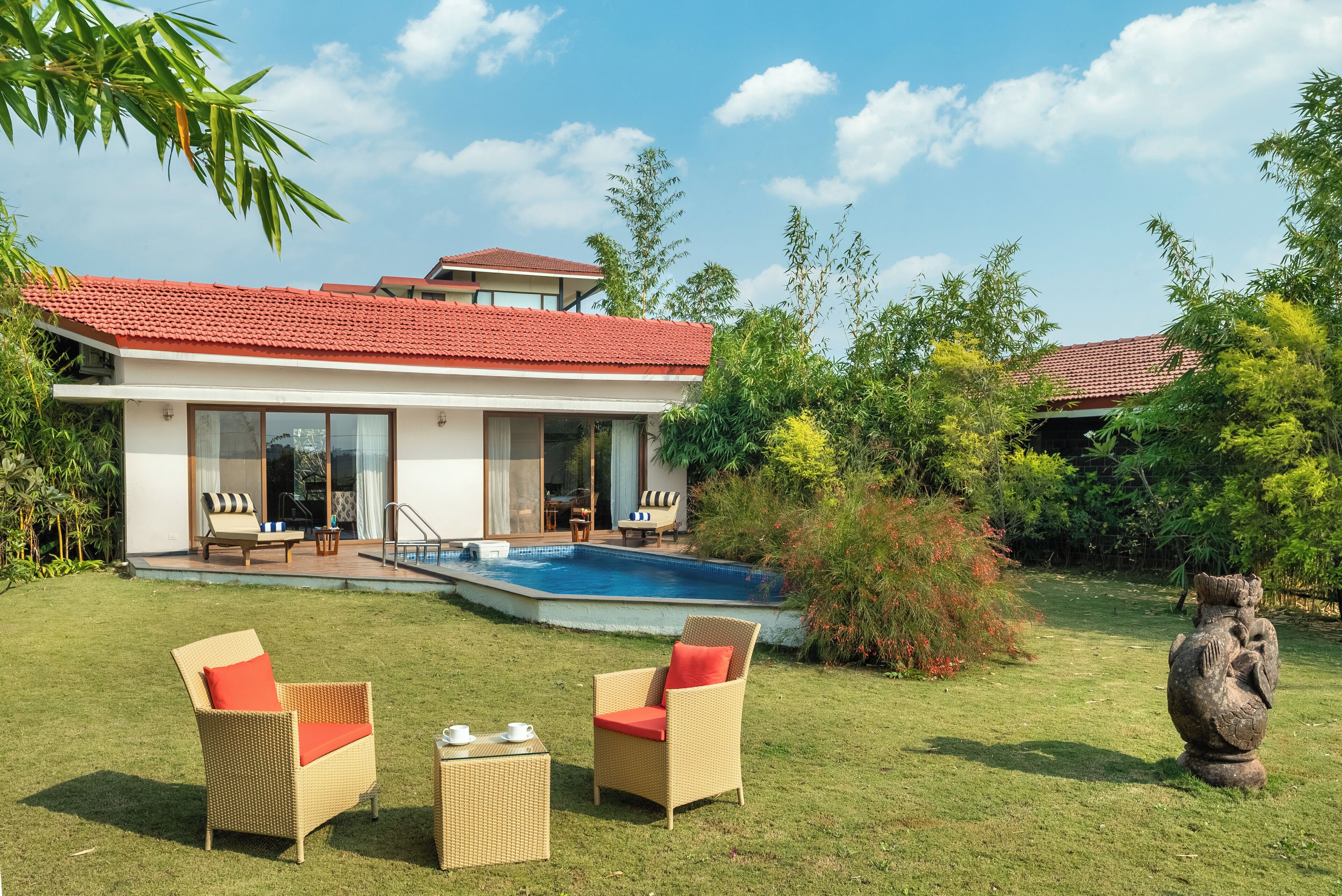 A modern house with a swimming pool, two wicker chairs, and a stone sculpture in the garden.