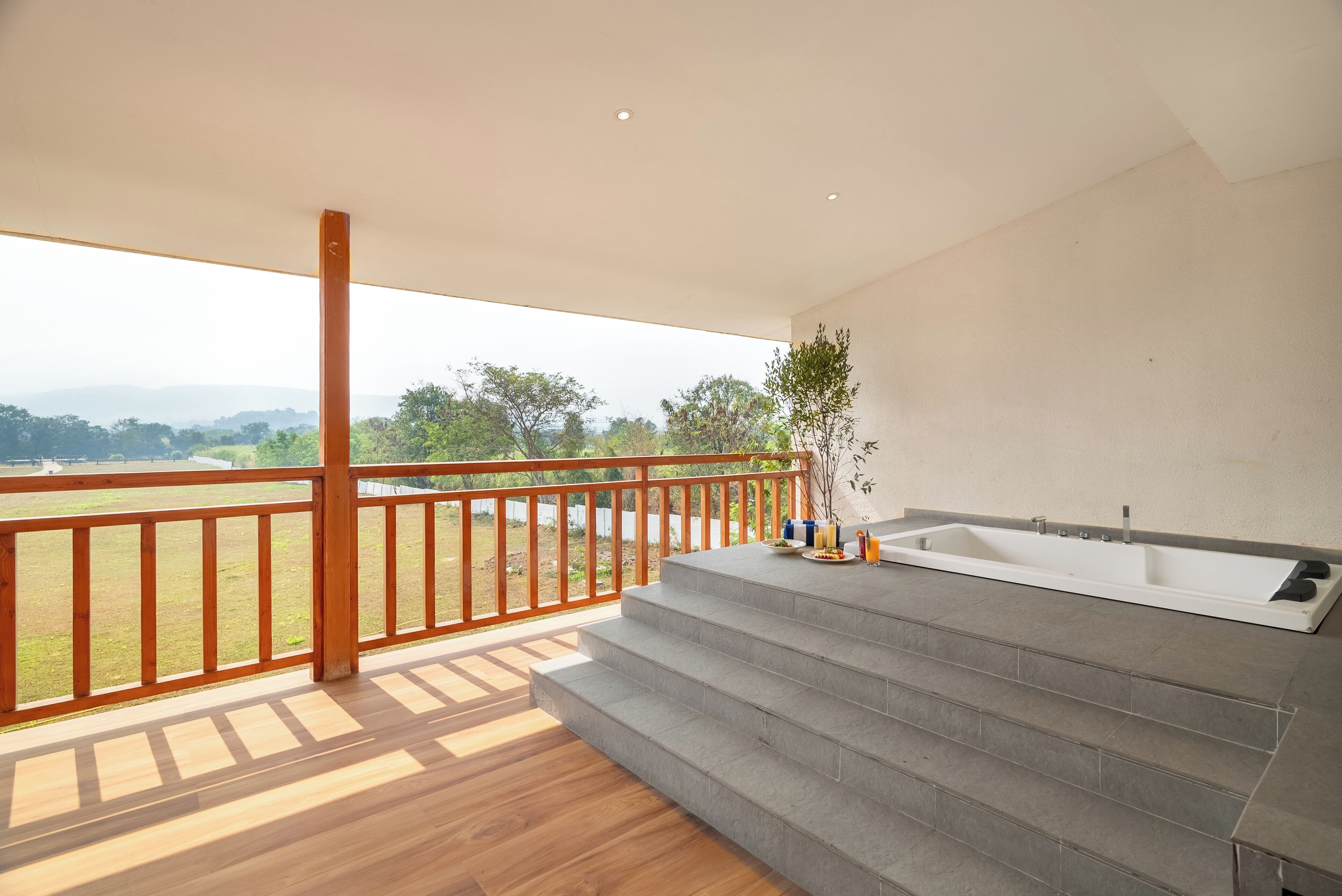 A modern bathroom with a large bathtub, wooden steps, and a view of a grassy field.