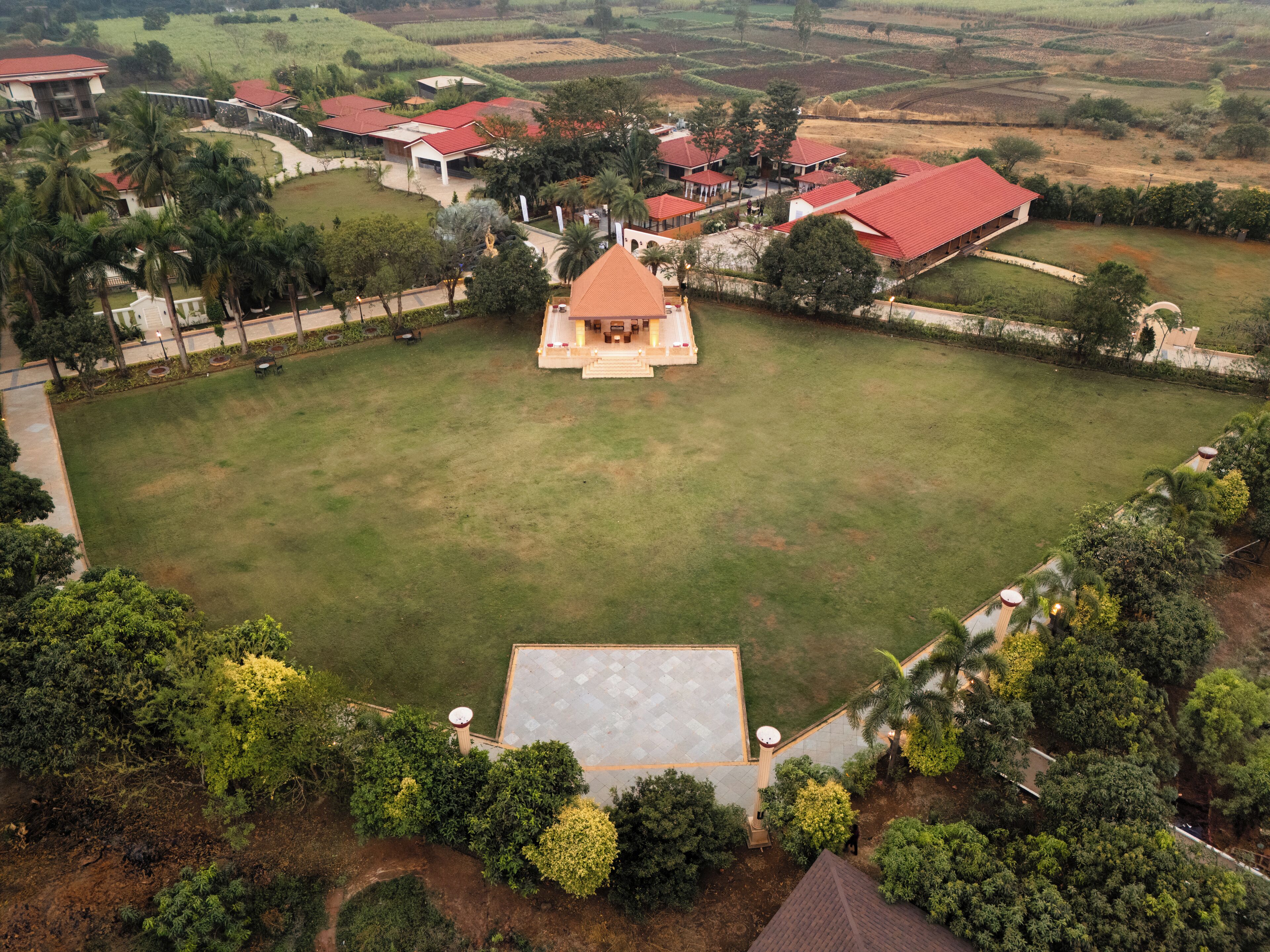 An aerial view of a residential area with multiple houses, a central open space, and surrounding greenery.
