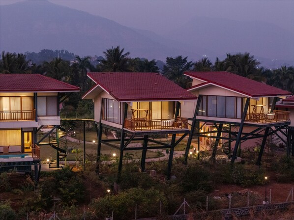 Una serie de estructuras de madera elevadas con balcones, rodeadas de exuberante vegetación y un telón de fondo montañoso.