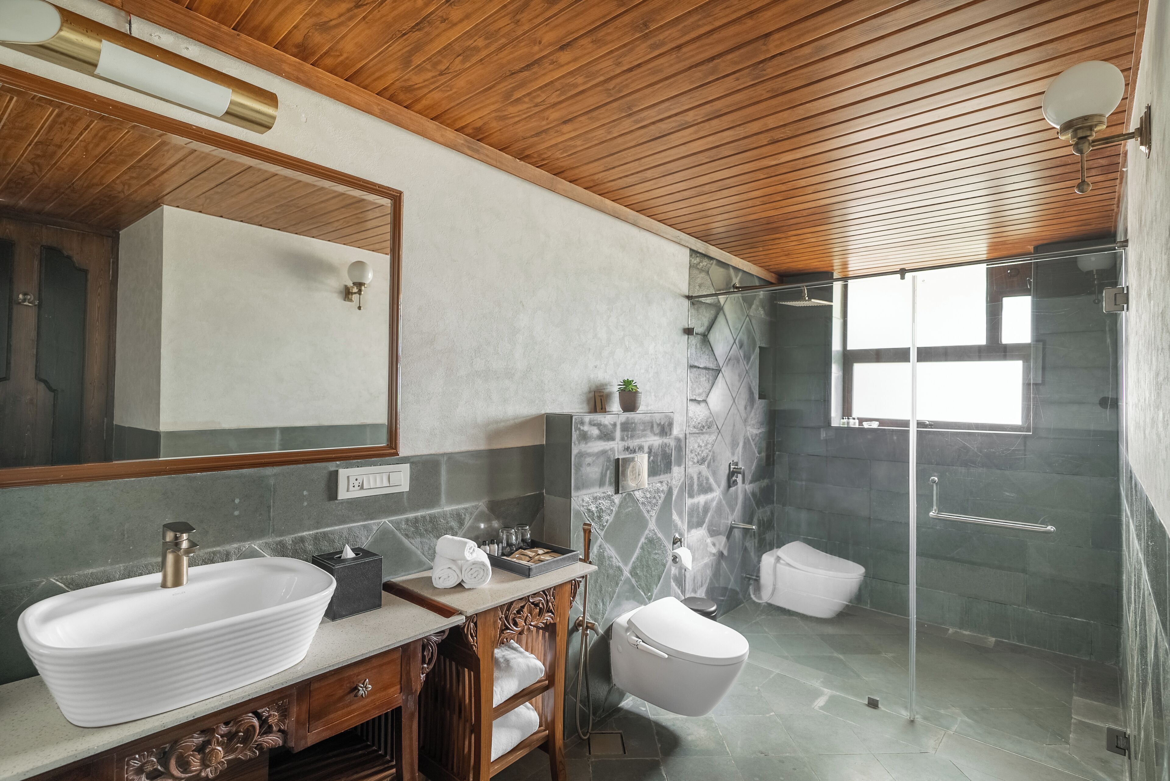 A modern bathroom with a large mirror, a vessel sink, a shower with a glass door, and a wooden ceiling.