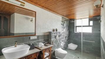 A modern bathroom with a large mirror, a vessel sink, a shower with a glass door, and a wooden ceiling.