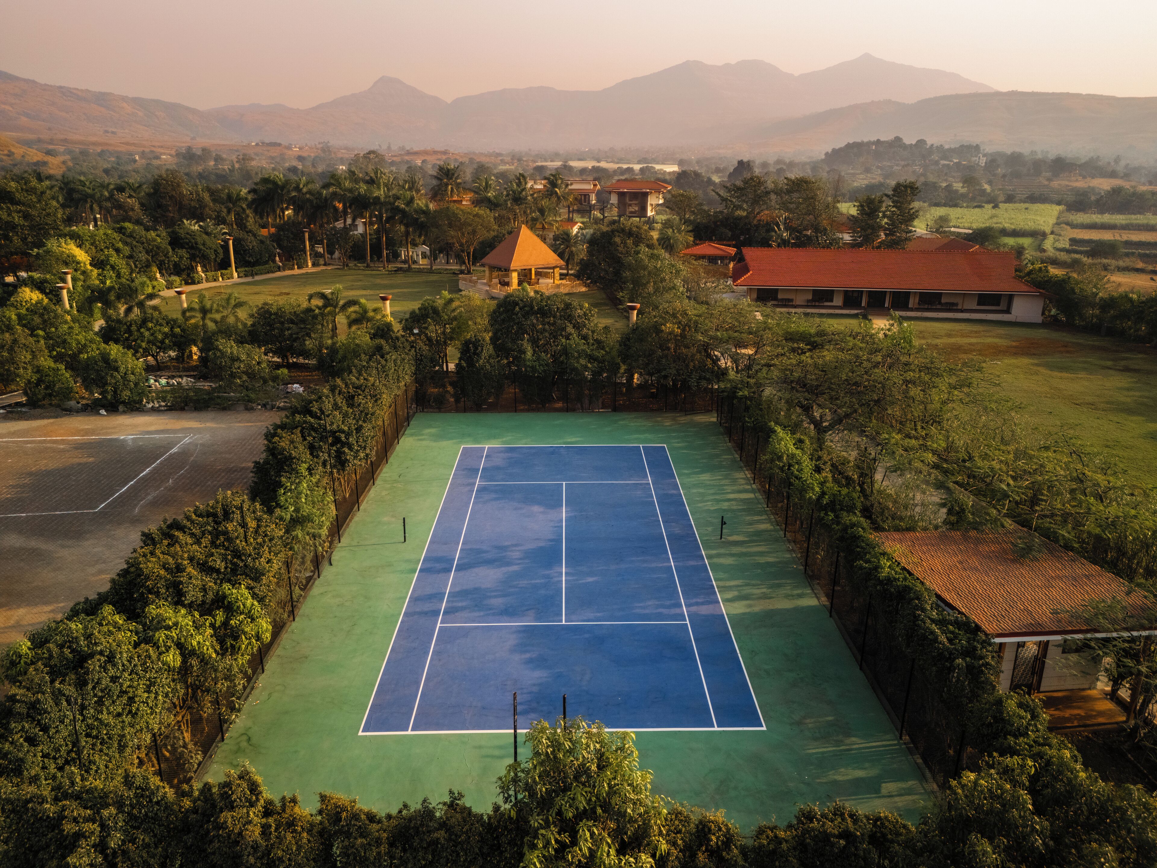 An aerial view of a tennis court surrounded by lush greenery and a mountainous backdrop.