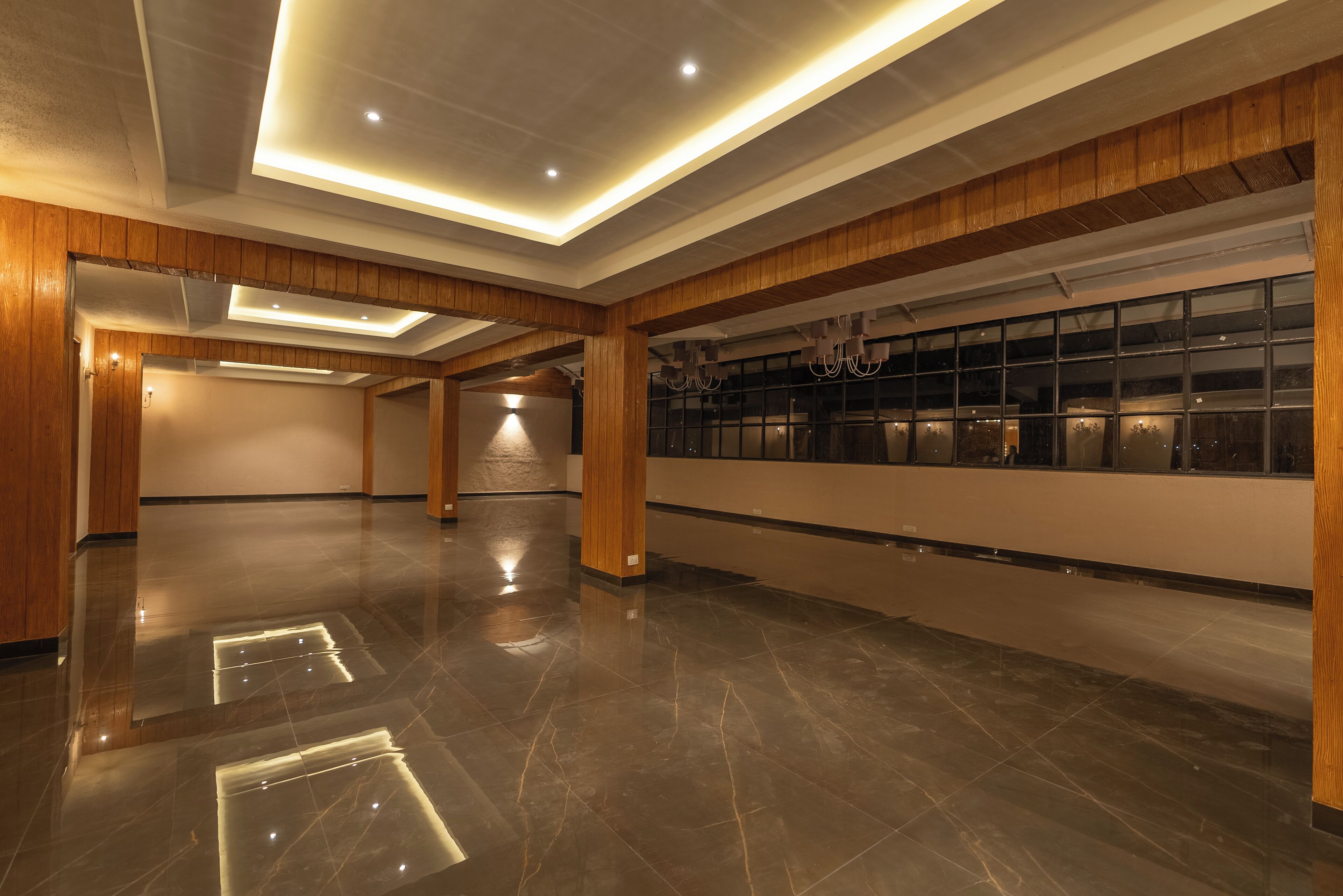 A spacious lobby with polished marble floors, wooden paneling, and a long wall with large windows.
