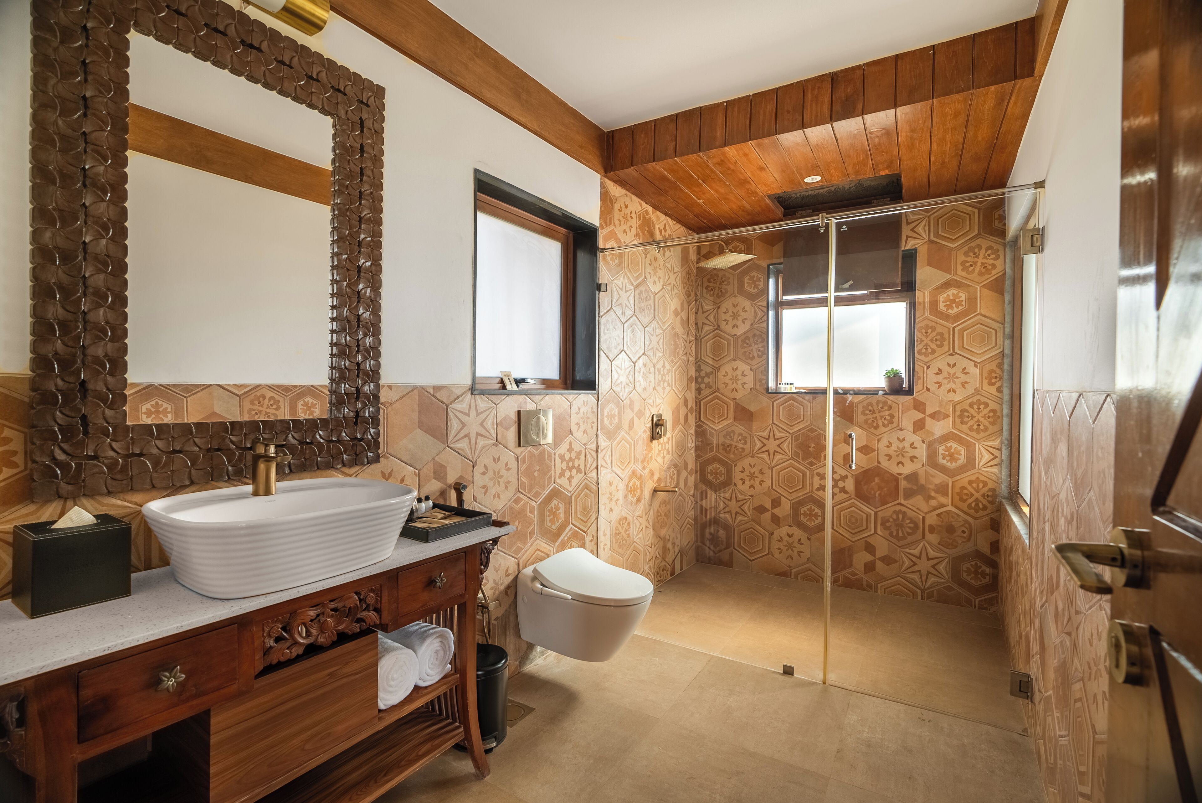 A modern bathroom with a large mirror, a white sink, a wooden vanity, a toilet, and a shower area with patterned tiles.