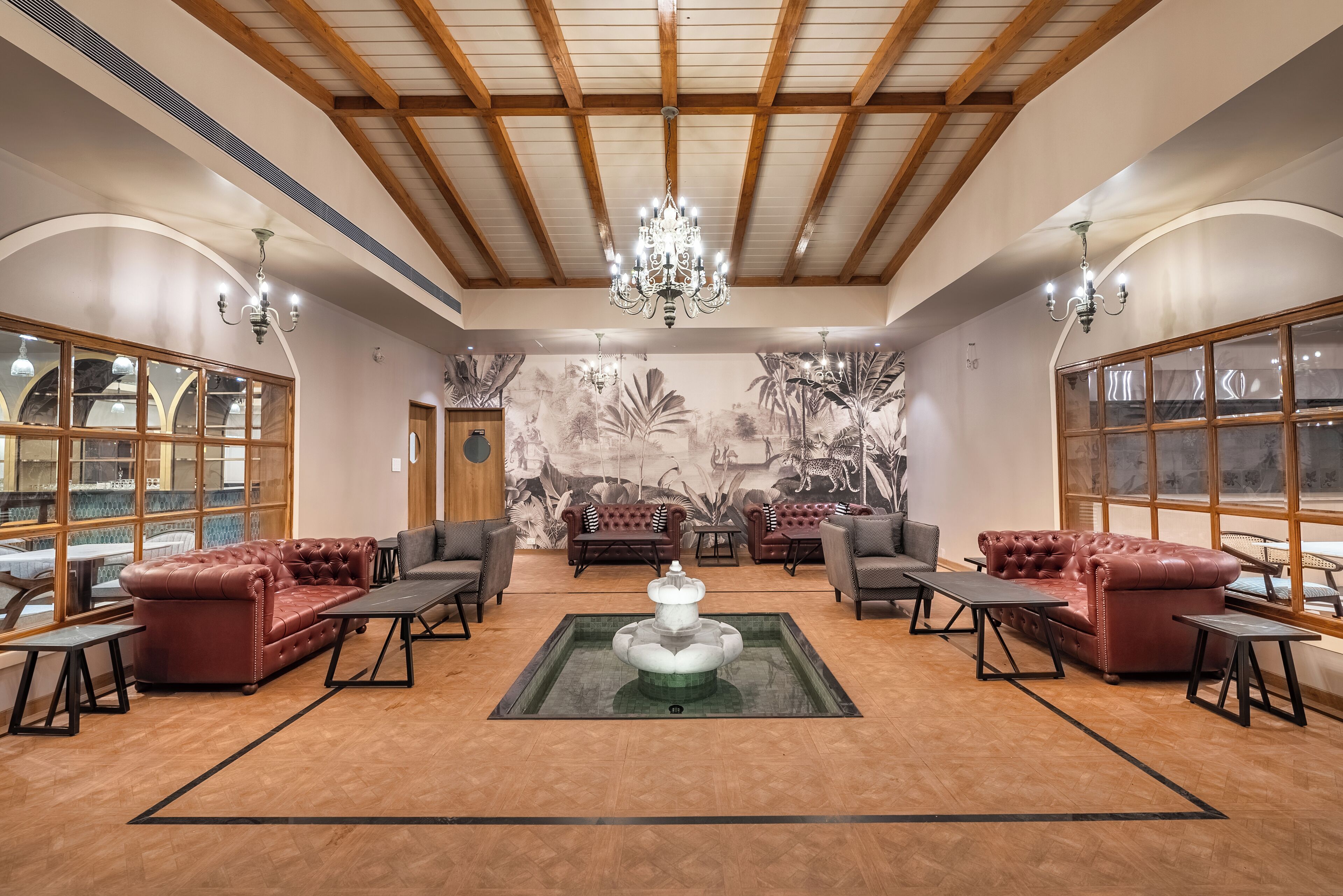 A spacious lobby with a central fountain, leather sofas, wooden flooring, and large windows.