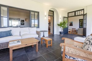 A spacious living area with a sofa, coffee table, and wicker chairs. - Zoete Zitje | Dual-home coastal escape in Voëlklip (Hermanus)