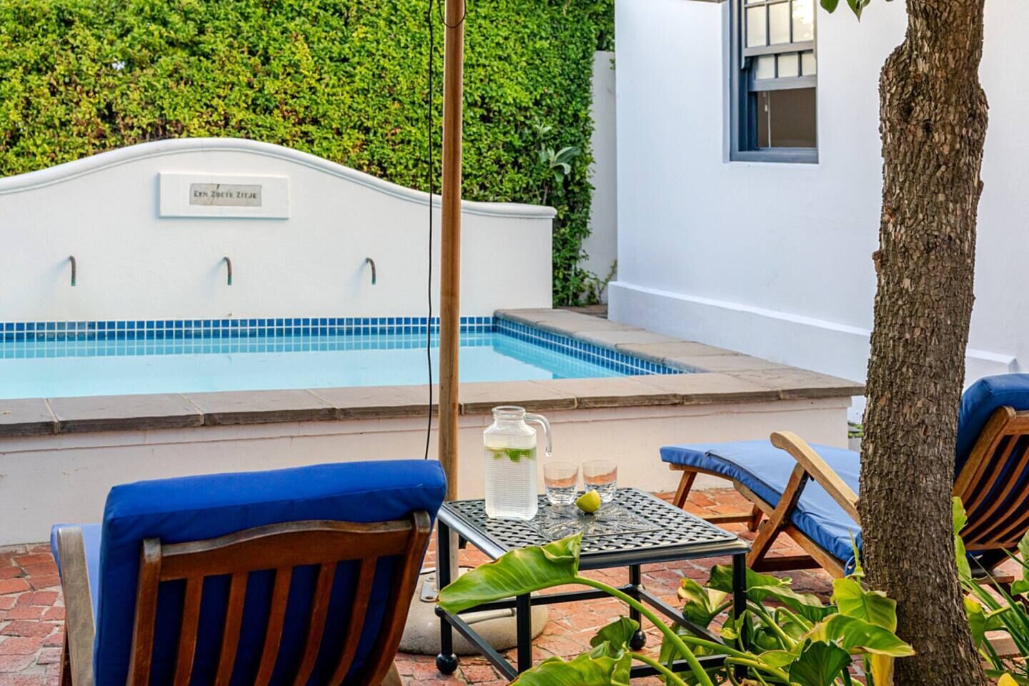 Ein Poolbereich mit weißer Wand, einem blau gefliesten Pool und zwei blauen Polsterstühlen.