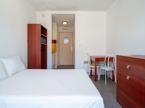 A hotel room with a bed, a wooden wardrobe, a desk with a chair, and a small kitchenette. - Charming studio for 2 people, pool view, balcony (Agde)