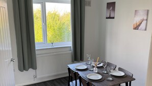 A dining area with a table set for four, a window with curtains, a radiator, and two framed pictures on the wall. - Rowe Terrace Workington (Workington)