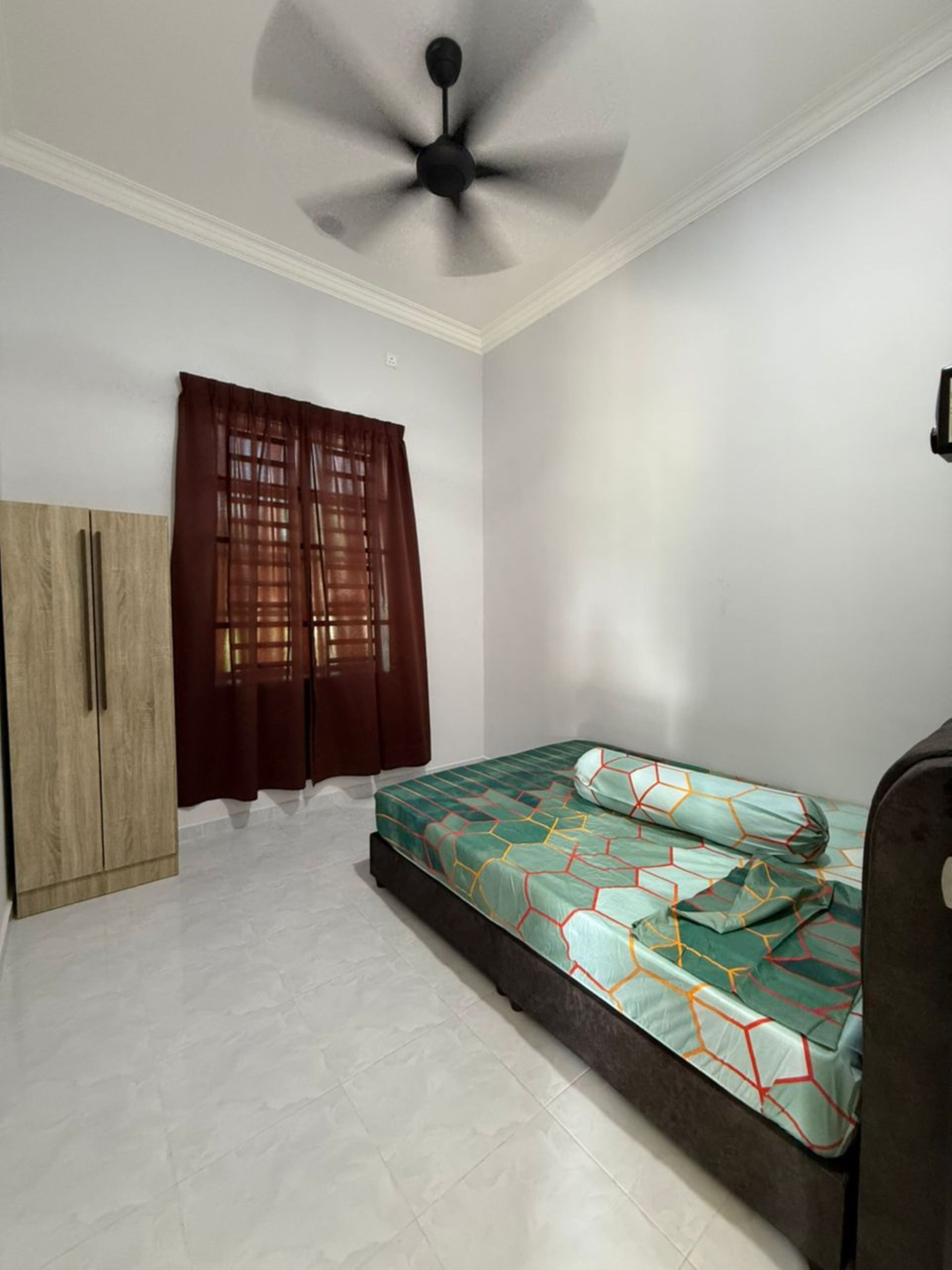 Un dormitorio con cama, armario, ventilador de techo y ventana con cortinas.