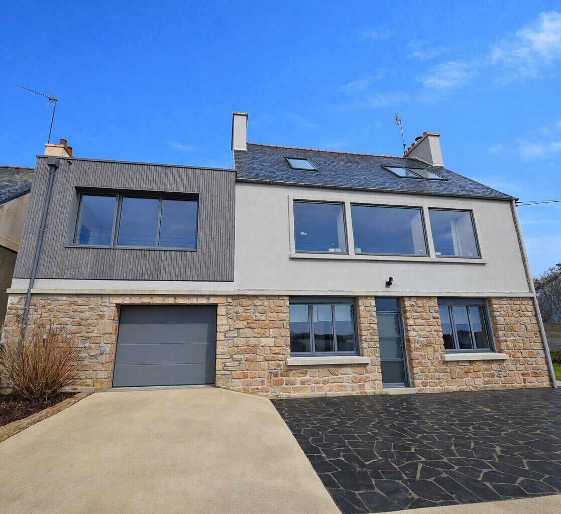 Une maison à deux étages avec un garage, une façade en pierre et un toit en pente.