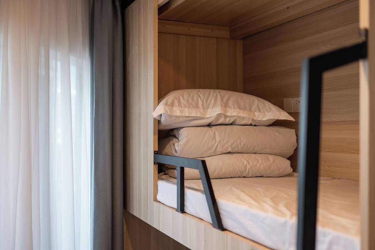 Un lit superposé avec une literie blanche, des murs en bois et une fenêtre ornée de rideaux légers.