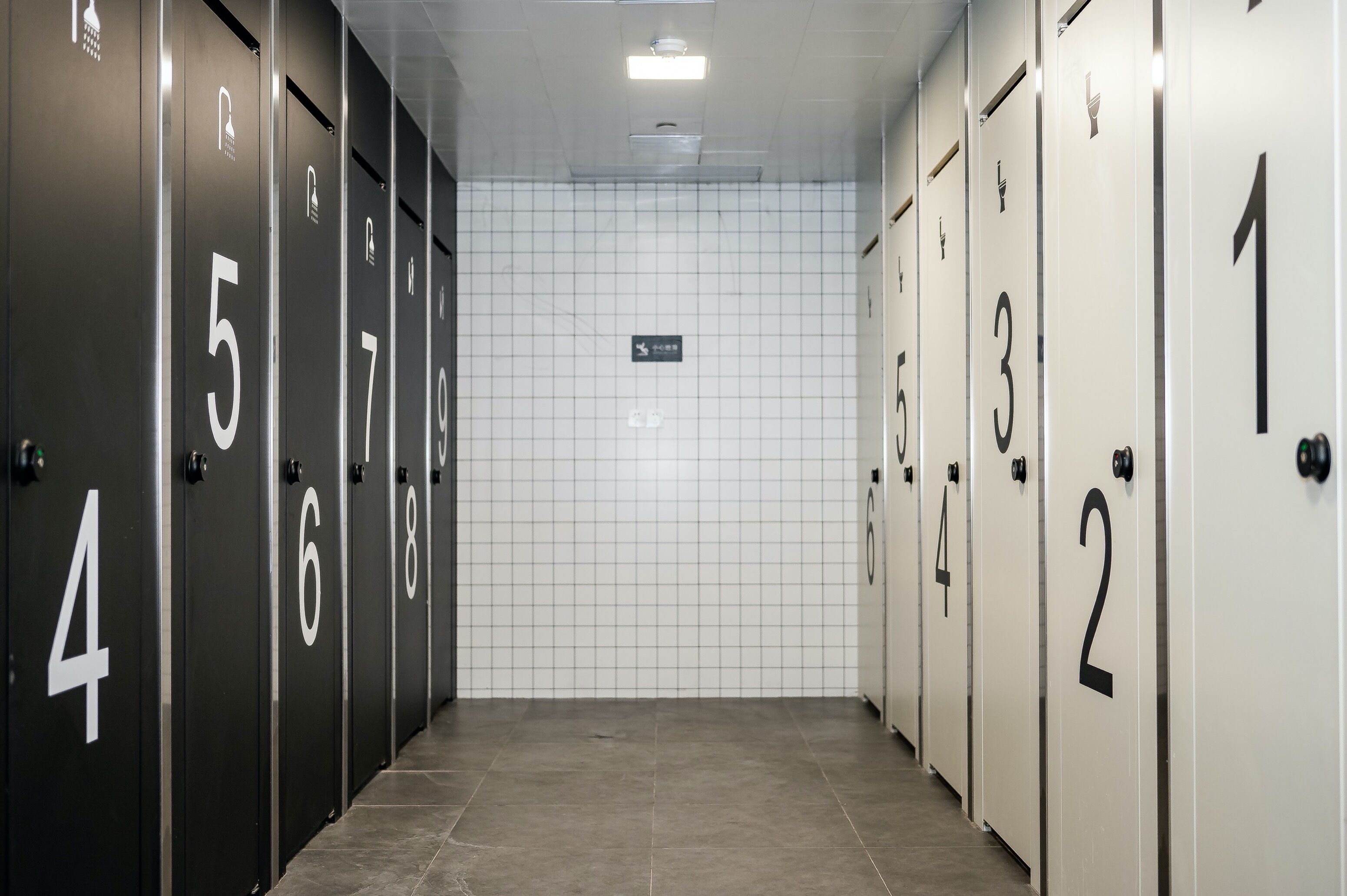 A row of numbered hotel rooms with a tiled wall and a sign indicating the direction to the bathroom.