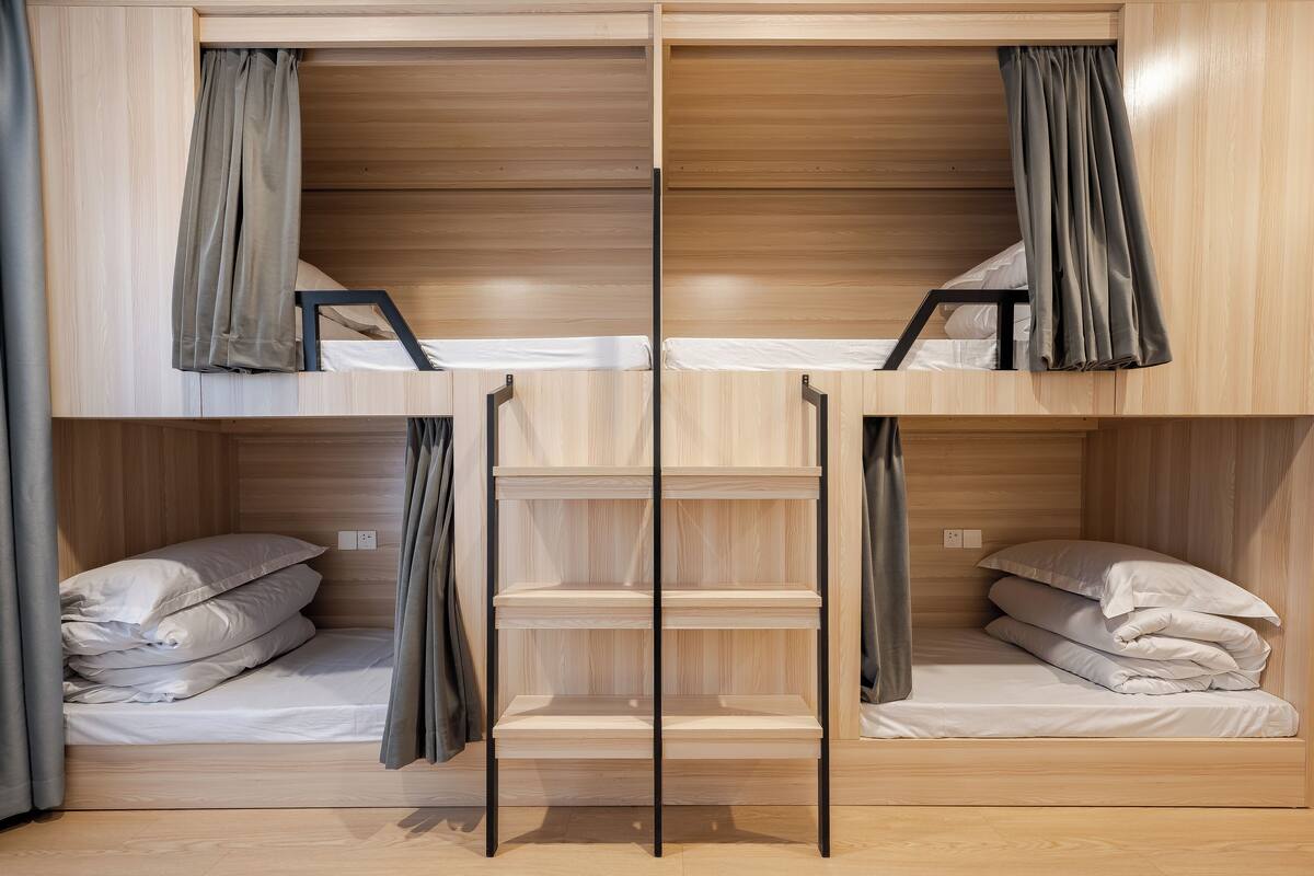 Une chambre avec un lit superposé, des murs en bois et des rideaux. Il y a deux lits, chacun avec un oreiller et une couverture.