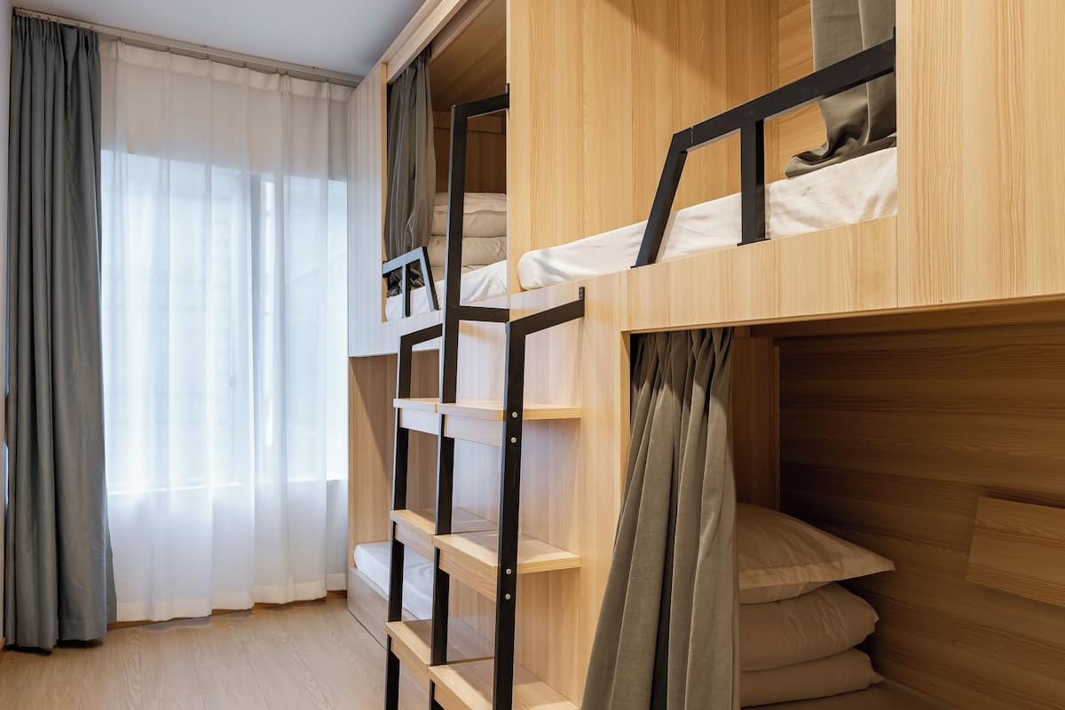 Une chambre avec des lits superposés, des murs en bois et une fenêtre ornée de rideaux légers.