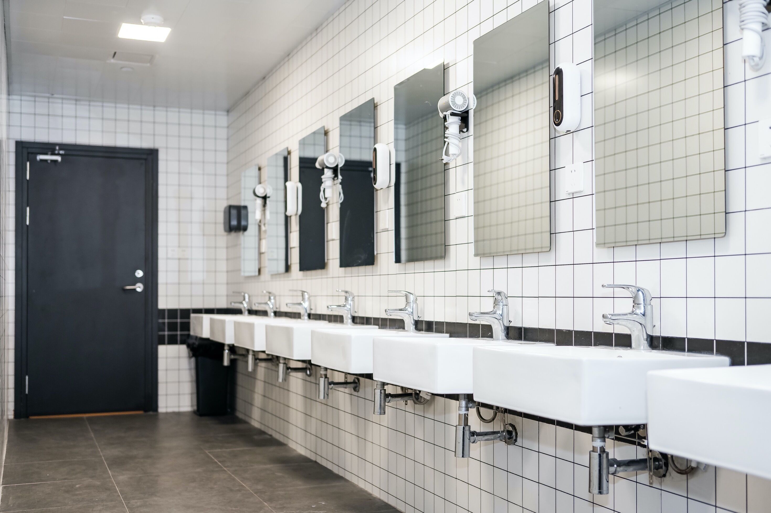 A public restroom with multiple sinks, mirrors, and a door.