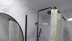 Une salle de bain avec un mur en marbre, un miroir rond, un lavabo blanc et une douche agrémentée d’un rideau de douche vert et blanc.