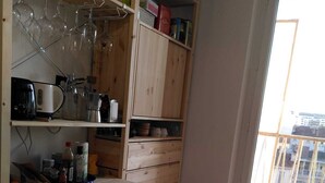 Une cuisine de taille réduite, dotée de meubles en bois, d’un plan de travail en marbre et d’une fenêtre donnant sur des immeubles.