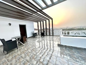 Terraza en la azotea con vistas a la ciudad al atardecer, diseño moderno que incluye una pérgola, zona de estar y una puerta.