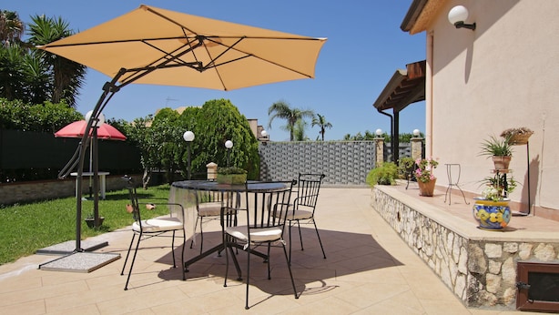 An outdoor patio with a round table and chairs, a large umbrella, and potted plants. - Spacious Villa with Garden, WiFI, A/C, Outdoor kitchen, short walk to the Sea (Piana Calzata)