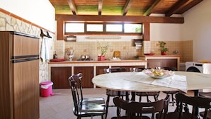 A kitchen with wooden beams, a dining table with chairs, a stove, and a washing machine. - Spacious Villa with Garden, WiFI, A/C, Outdoor kitchen, short walk to the Sea (Piana Calzata)