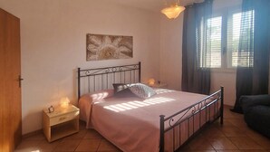 A bedroom with a bed, nightstands, a lamp, a painting, and a window with curtains. - Spacious Villa with Garden, WiFI, A/C, Outdoor kitchen, short walk to the Sea (Piana Calzata)