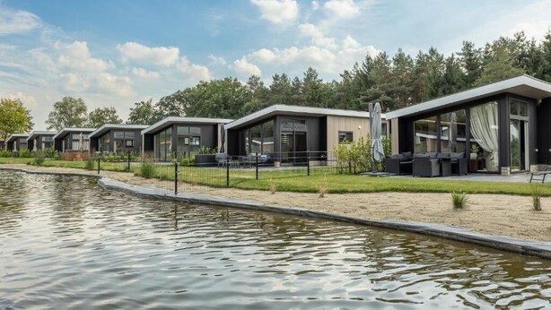 A row of modern, single-story buildings with large windows, a small pond in the foreground, and a clear sky. - Residence Winterswijk (Winterswijk - Huppel)