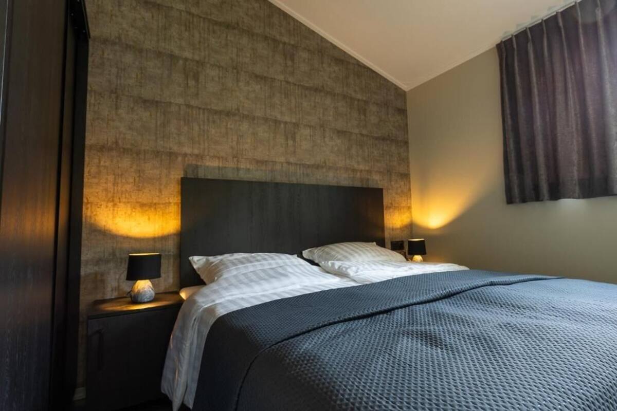 Een moderne hotelkamer met een groot bed, twee nachtkastjes met lampen, en een structuurwand.