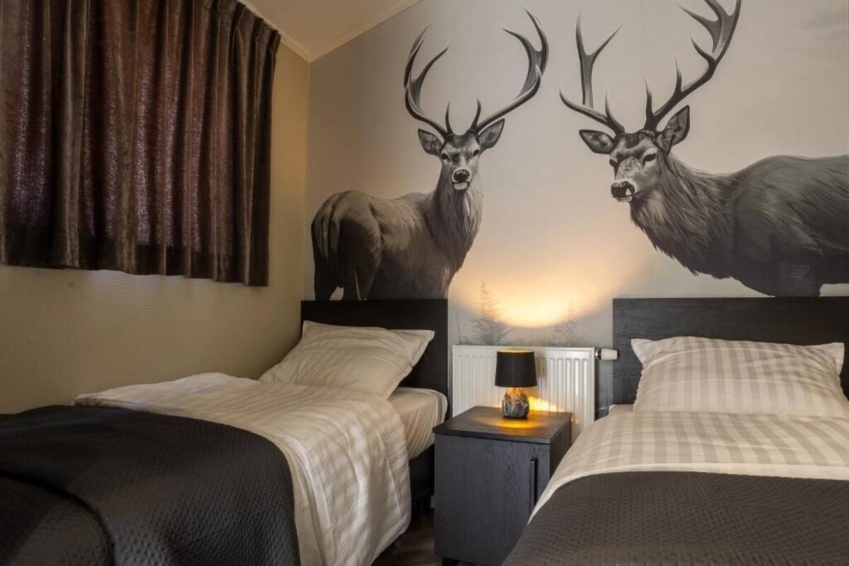 Een hotelkamer met twee bedden, een nachtkastje met een lamp en een wanddecoratie van herten.