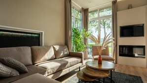 A modern living room with a beige sofa, a round wooden coffee table, and a TV mounted on the wall. - Residence Winterswijk (Winterswijk - Huppel)