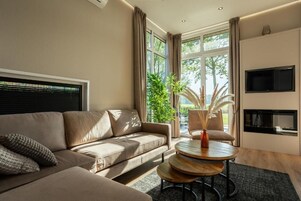 Un salón moderno con un sofá color beige, una mesa de centro redonda de madera y un televisor montado en la pared.