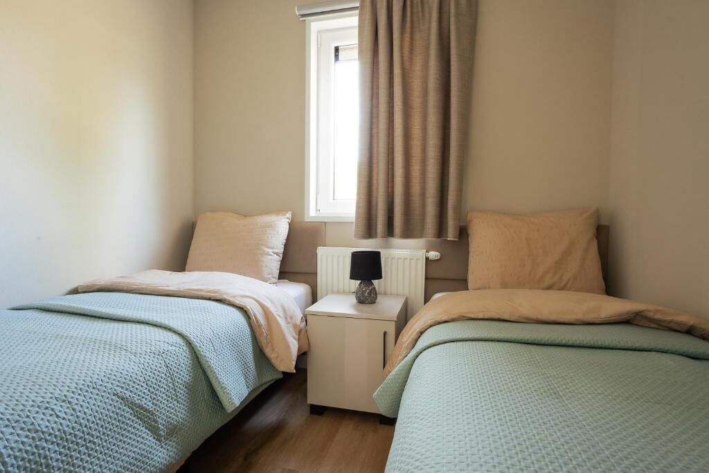 A small, cozy bedroom with two single beds, a nightstand with a lamp, and a window with curtains.