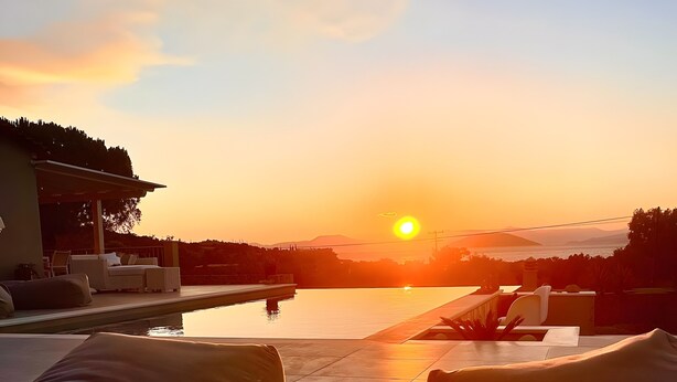 A poolside lounge area with sun loungers and a table, overlooking a body of water and a sunset. - Luxury & Romantic Escape – Ideal for Couples & Newlyweds (Kranidi)
