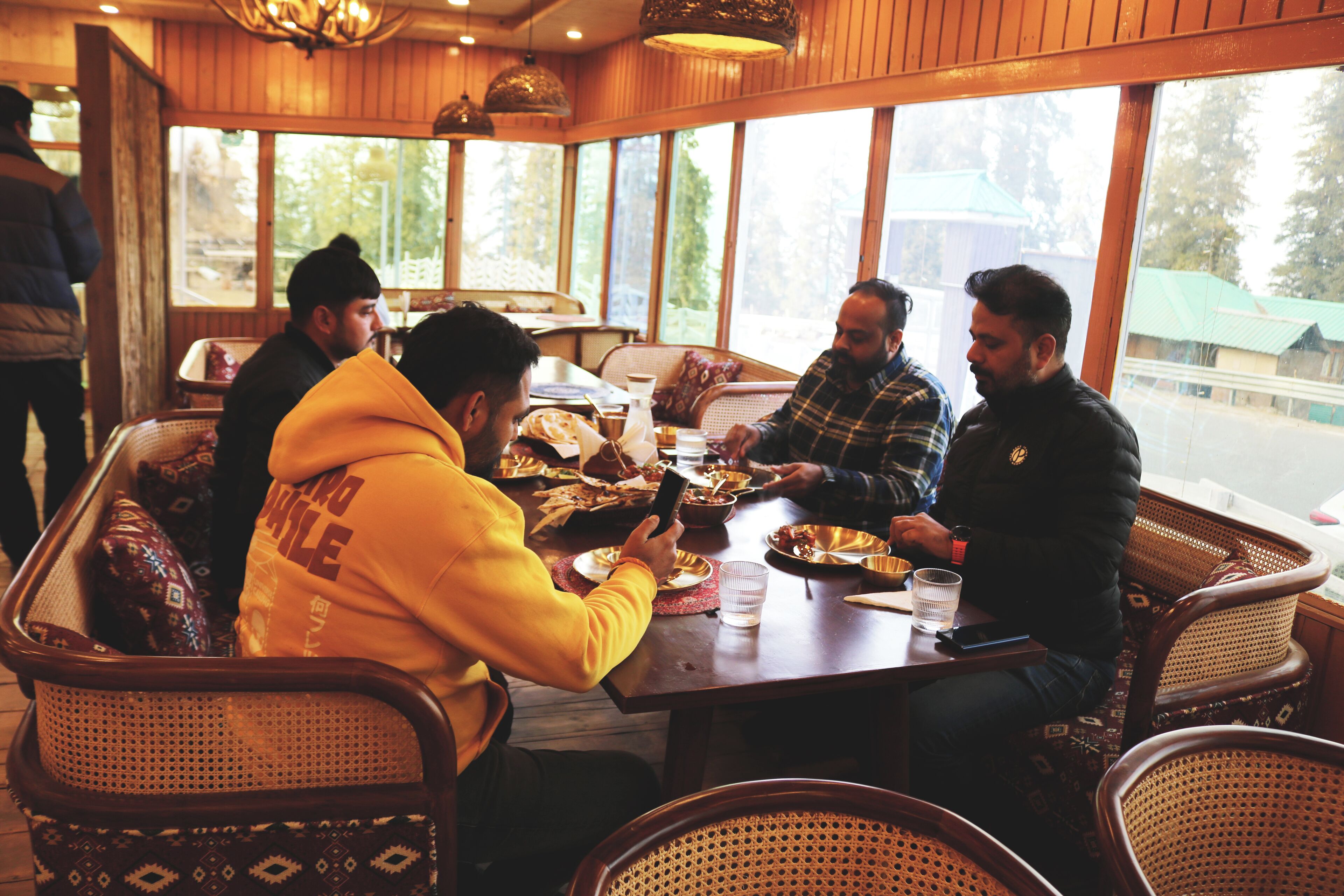 A group of people dining at a wooden table with a view of trees outside.