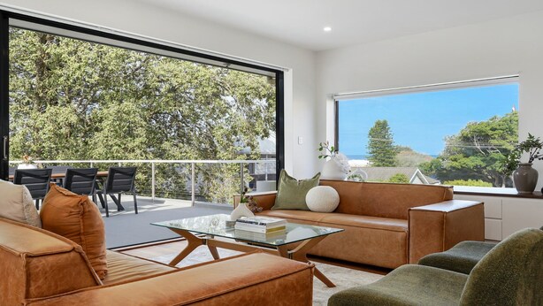 A modern living room with a glass coffee table, leather sofas, and a view of trees and a clear sky.