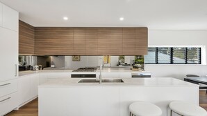A modern kitchen with white cabinetry, a central island with stools, and a large window providing natural light.