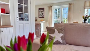 Un salon avec un canapé beige, un coussin orné d’un motif en étoile et une fenêtre avec des rideaux.