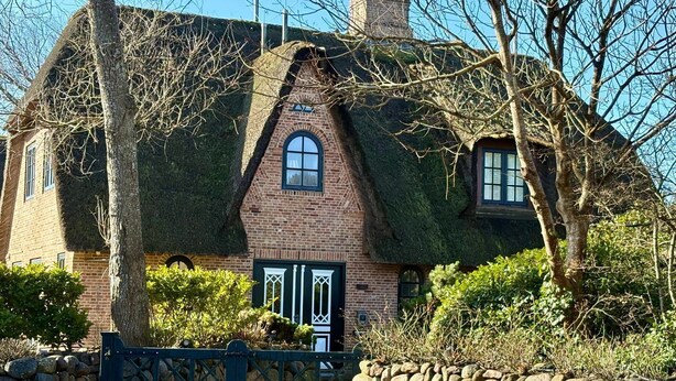Une maison traditionnelle en briques, avec un toit de chaume, un mur en pierre et une entrée fermée par un portail.