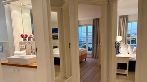 Une chambre d’hôtel avec une grande fenêtre, un lit, une table de chevet et une salle de bain équipée d’un lavabo et d’un miroir.