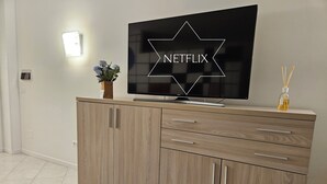 Ein modernes Wohnzimmer mit einem an der Wand montierten Flachbildfernseher, einer Wandleuchte und einer kleinen Vase mit Blumen.