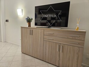 Ein modernes Wohnzimmer mit einem an der Wand montierten Flachbildfernseher, einer Wandleuchte und einer kleinen Vase mit Blumen.