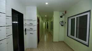 Un pasillo con suelo de madera, paredes blancas con franjas negras, un ascensor negro y una ventana con reja de metal.