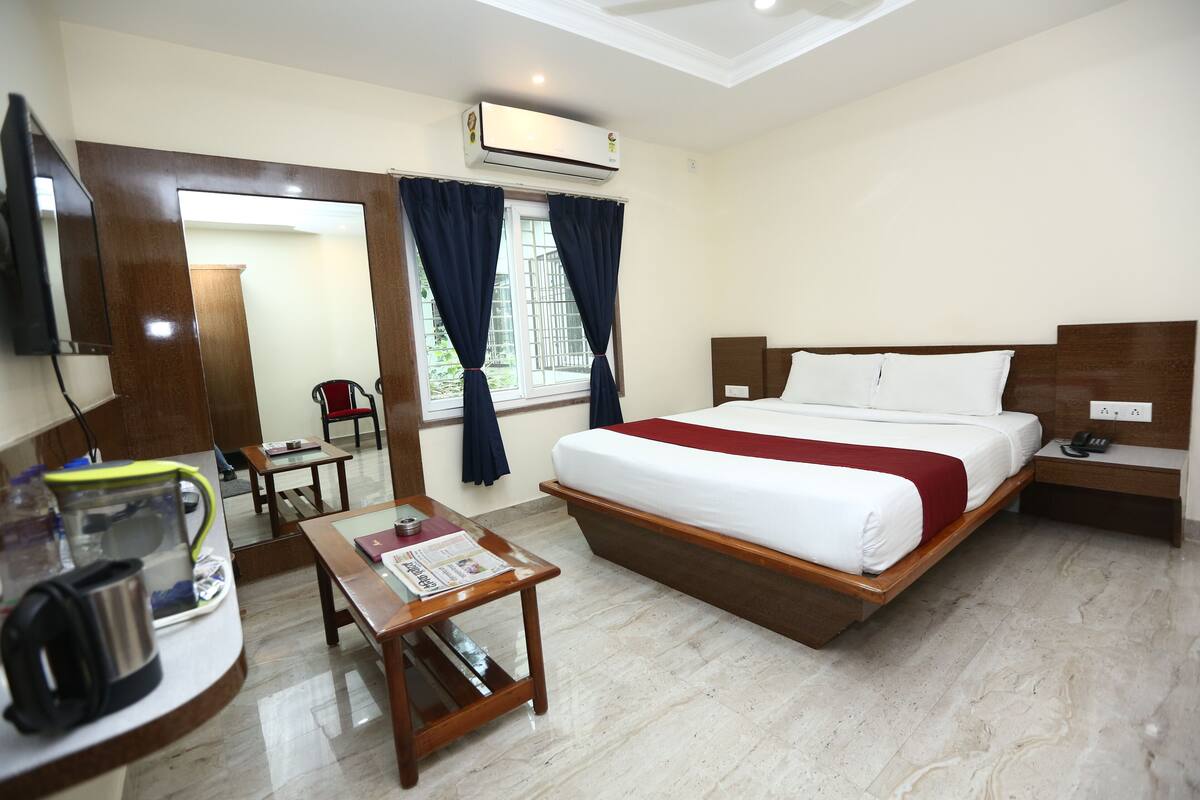 A hotel room with a bed, a desk, a chair, an air conditioner, and a window with curtains.