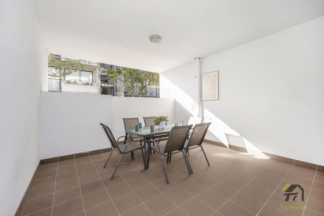 A spacious balcony with a dining table and chairs, a view of the neighborhood, and a staircase leading to an upper floor.