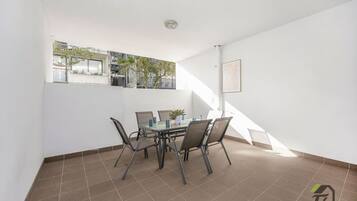 A spacious balcony with a dining table and chairs, a view of the neighborhood, and a staircase leading to an upper floor.