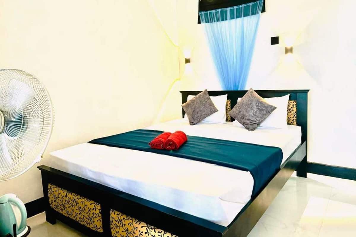 A neatly made bed with a green bedspread, two pillows, and a pair of red towels.