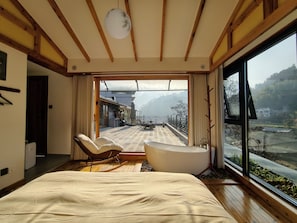 Ein Schlafzimmer mit einem großen Bett, einer Sitzecke mit einem Sessel, einer Badewanne und Blick auf eine Berglandschaft durch ein großes Fenster.
