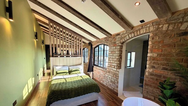 Un dormitorio con una cama grande, vigas de madera, paredes de ladrillo y vistas al exterior.