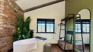Un baño moderno con una bañera independiente, un espejo grande y una ventana con vista a árboles.